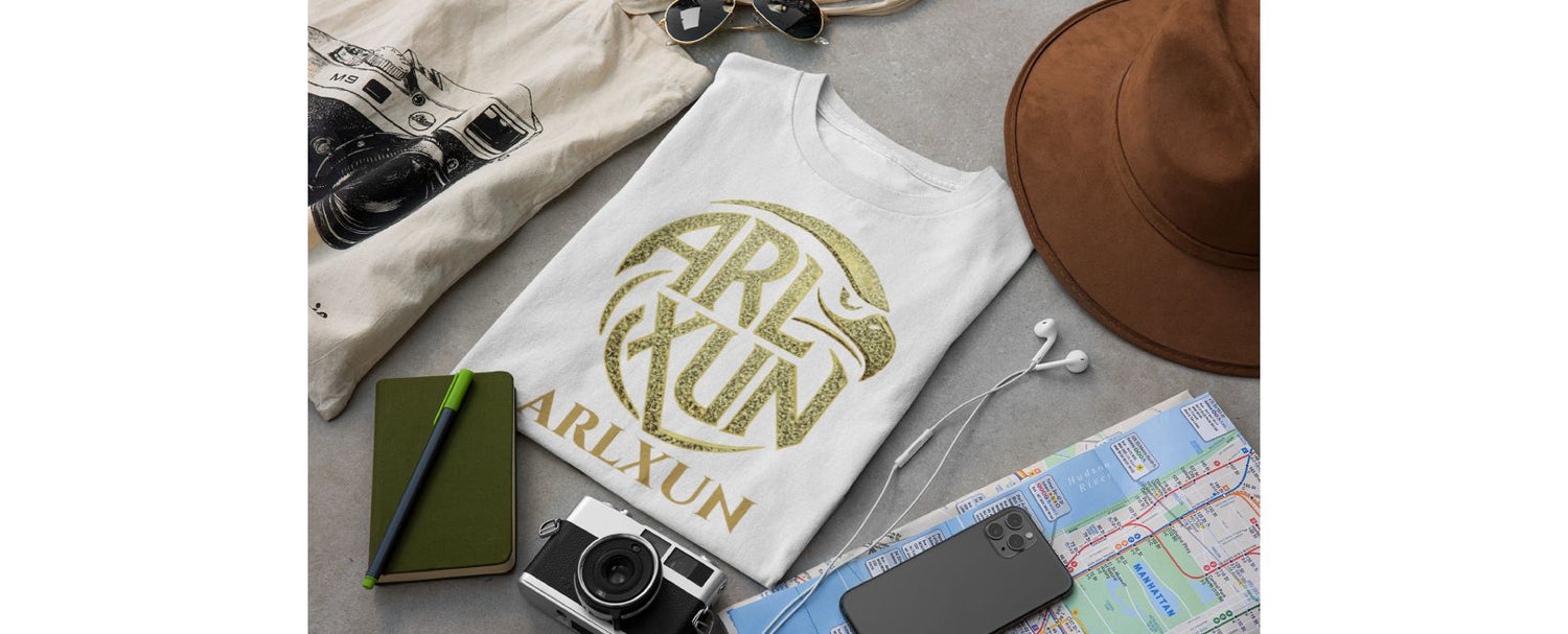 White t-shirt with 'ARLXUN' design on a surface with travel items.